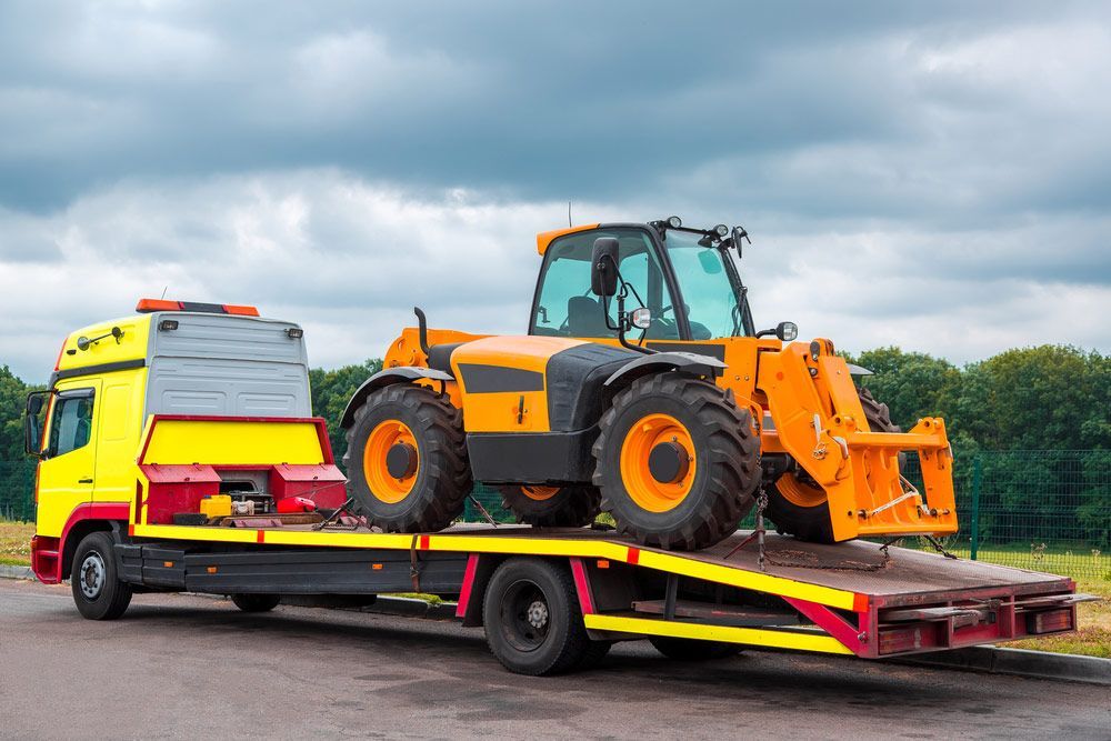 A Yellow Tractor Is Being Towed By A Tow Truck — Gympie/Childers Towing Pty Ltd in Sunshine Coast, QLD