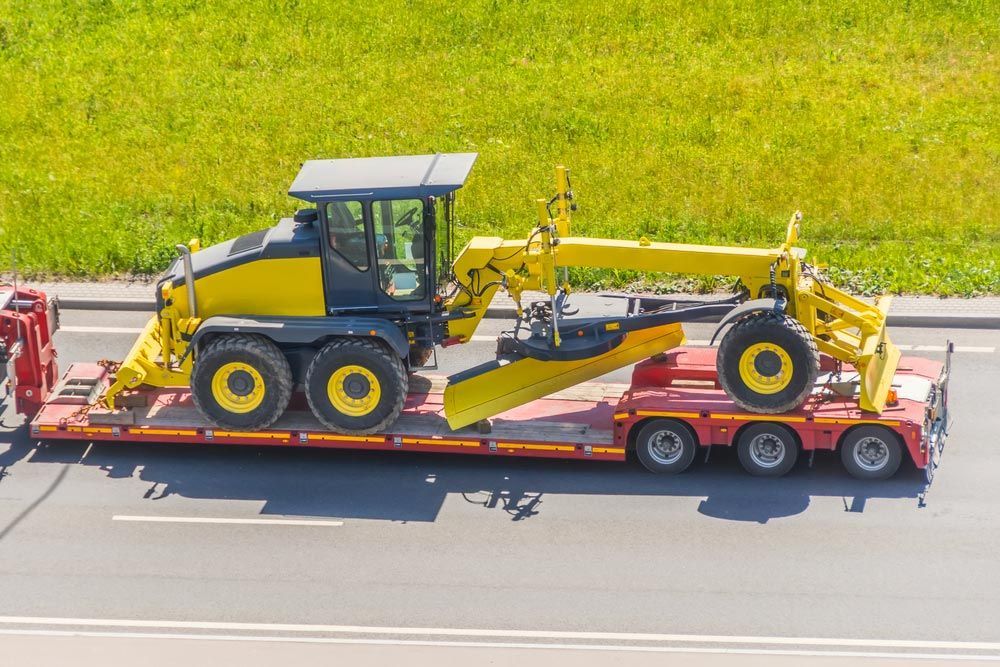 A Yellow Tractor Is Being Transported On A Trailer On A Highway — Gympie/Childers Towing Pty Ltd in Gympie, QLD