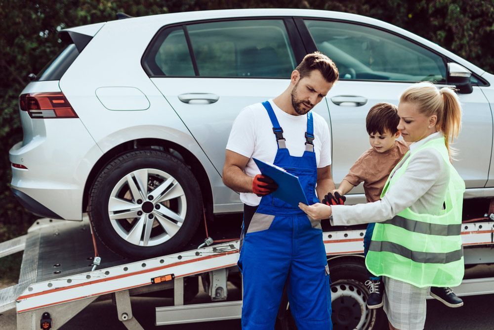 A Man And A Woman Are Standing Next To A Tow Truck With A Car On It — Gympie/Childers Towing Pty Ltd in Brisbane, QLD