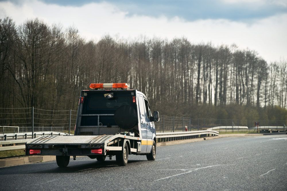 A Tow Truck Is Driving Down A Highway Next To A Forest — Gympie/Childers Towing Pty Ltd in Childers, QLD