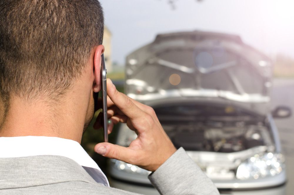 A Man Is Talking On A Cell Phone In Front Of A Broken Down Car — Gympie/Childers Towing Pty Ltd in Sunshine Coast, QLD