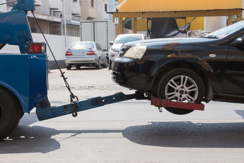 A Black Car Is Being Towed By A Blue Tow Truck — Gympie/Childers Towing Pty Ltd in Childers, QLD