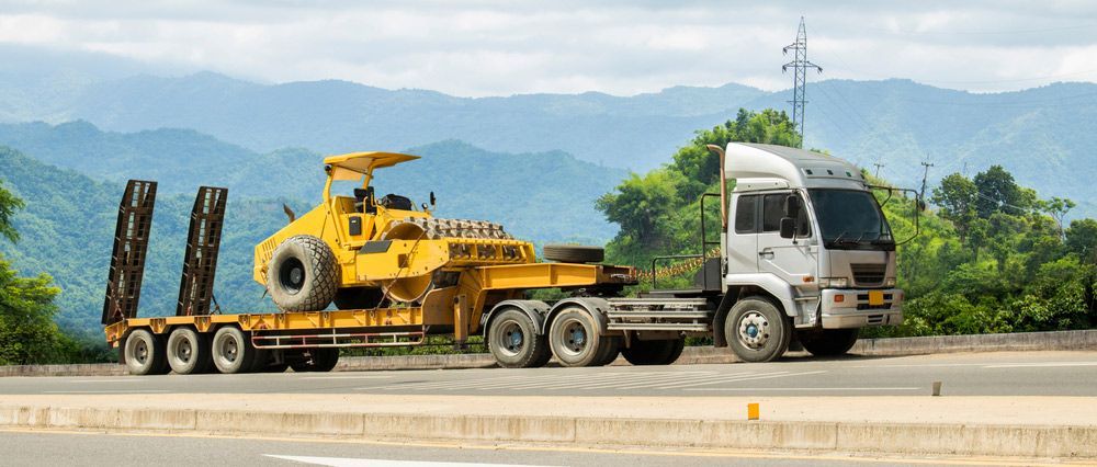 A Truck Is Carrying A Yellow Bulldozer On A Trailer On A Highway — Gympie/Childers Towing Pty Ltd in Brisbane, QLD