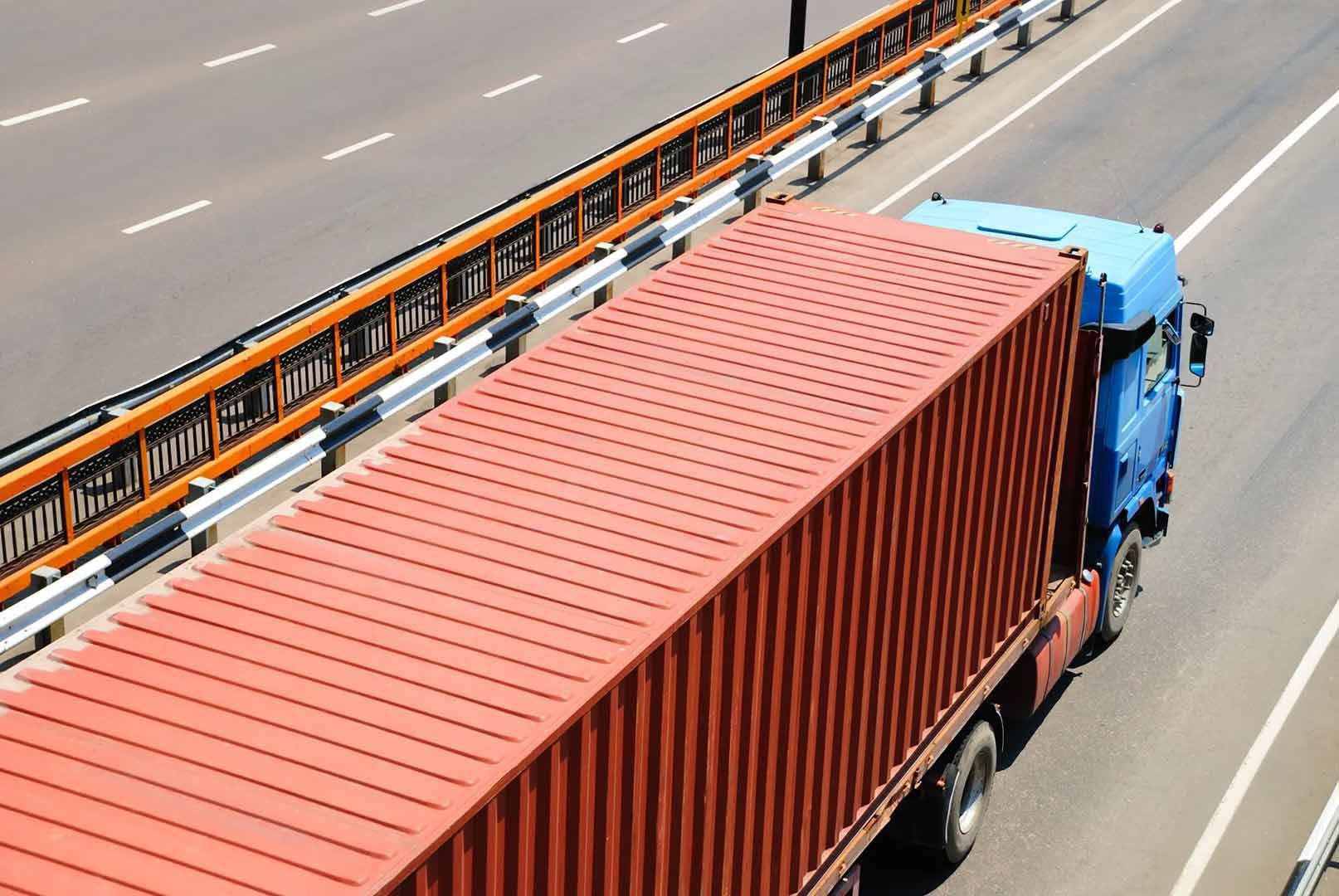 A Red Container Truck Is Driving Down A Highway — Gympie/Childers Towing Pty Ltd in Kybong, QLD