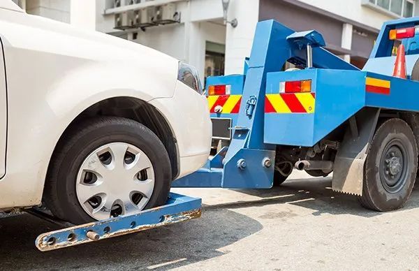 A White Car Is Being Towed By A Blue Tow Truck — Gympie/Childers Towing Pty Ltd in Kybong, QLD