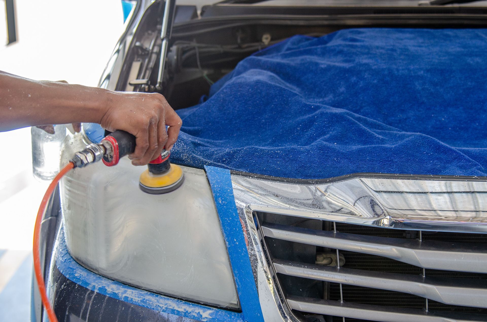 Hand polishing a car headlight with a buffer, blue towel covering the hood.