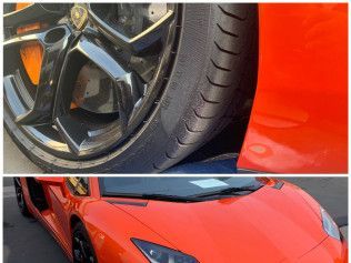 Close-up of a black wheel on a red sports car, with the hood and front end visible.