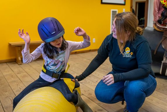 A woman is helping a little girl ride a yellow balancing peanut.