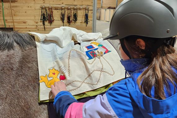 A young girl wearing a helmet is petting a brown horse in a stable.