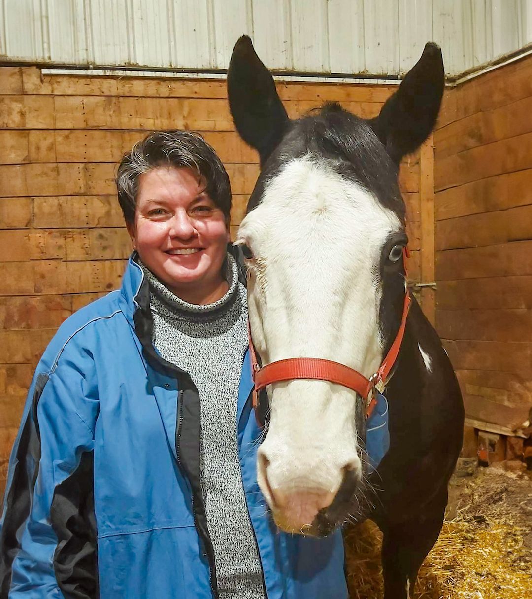 A woman in a blue jacket is standing next to a black and white horse.