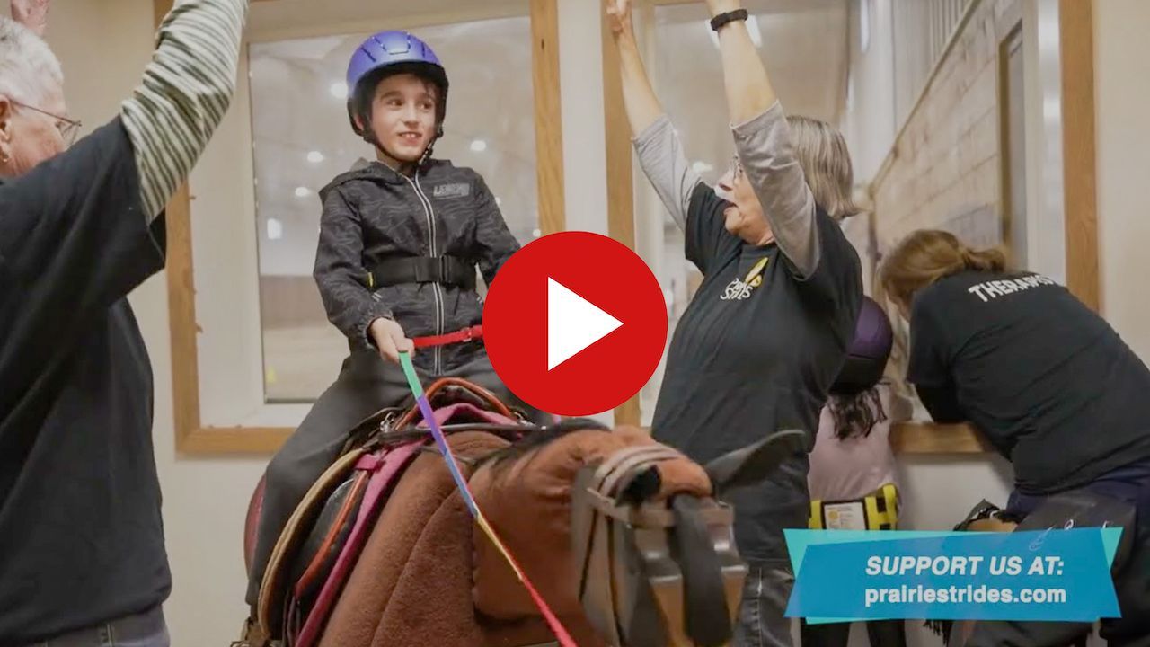 Screen capture from video of child riding an Equicizer horse with helpers
