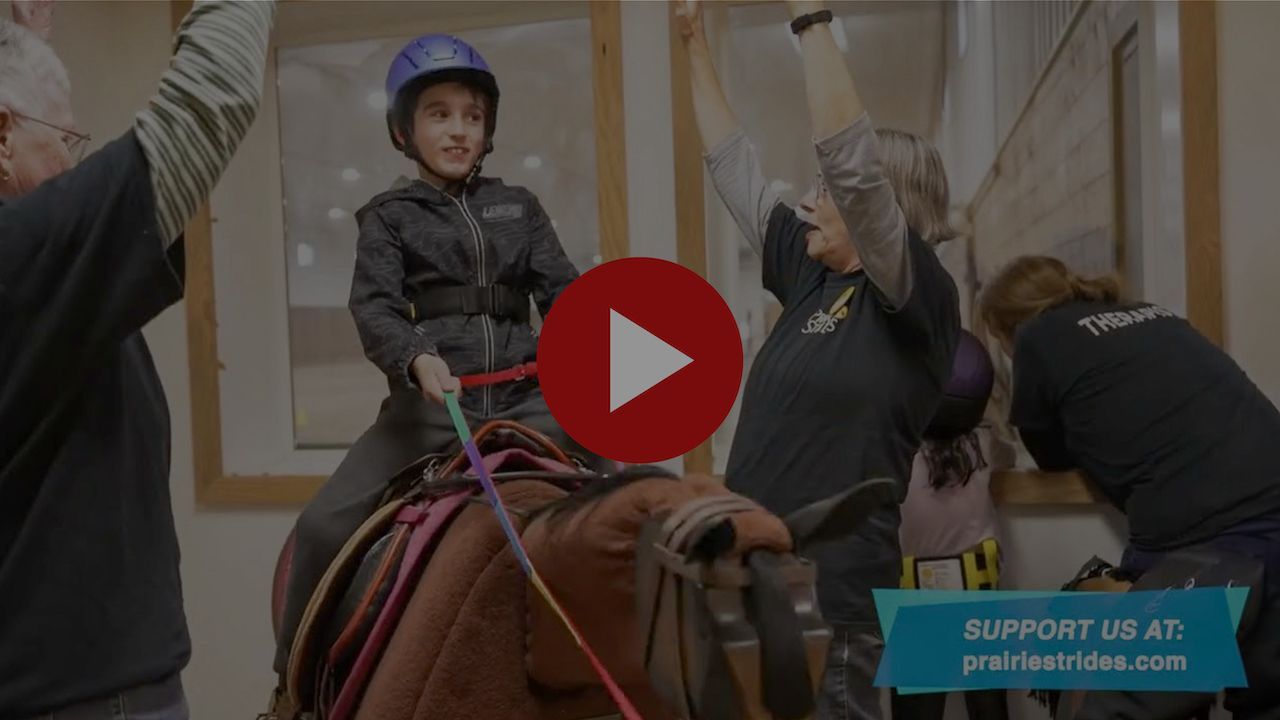 Screen capture from video of child riding an Equicizer horse with helpers