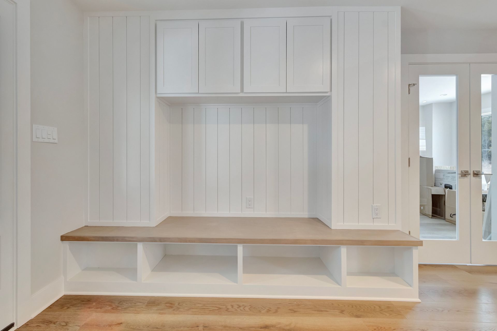 White built-in storage unit with cabinets, bench, and cubbies; located in a hallway with a door.