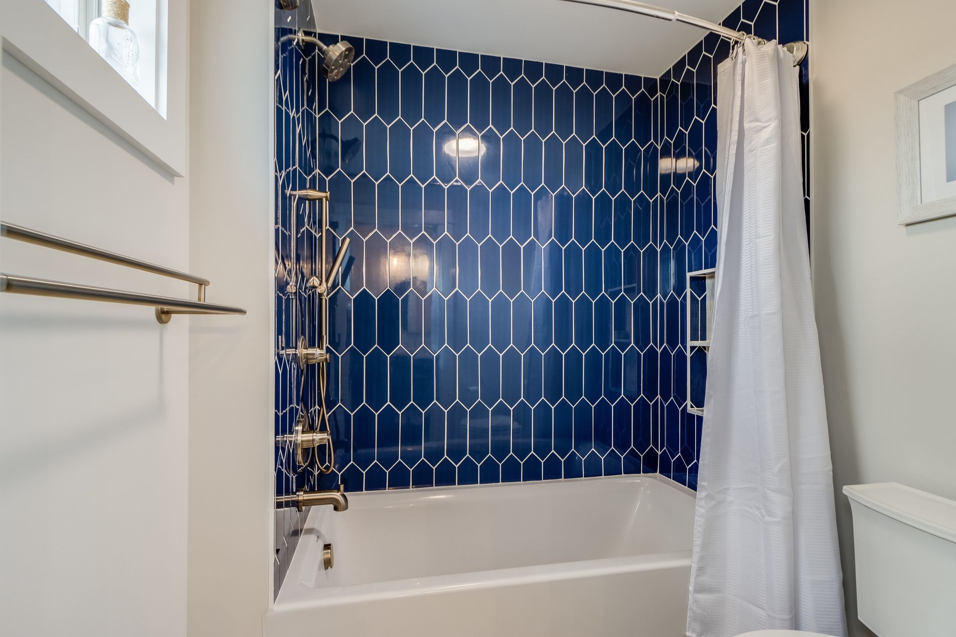 Blue tiled shower with silver fixtures, white curtain, and a white bathtub.