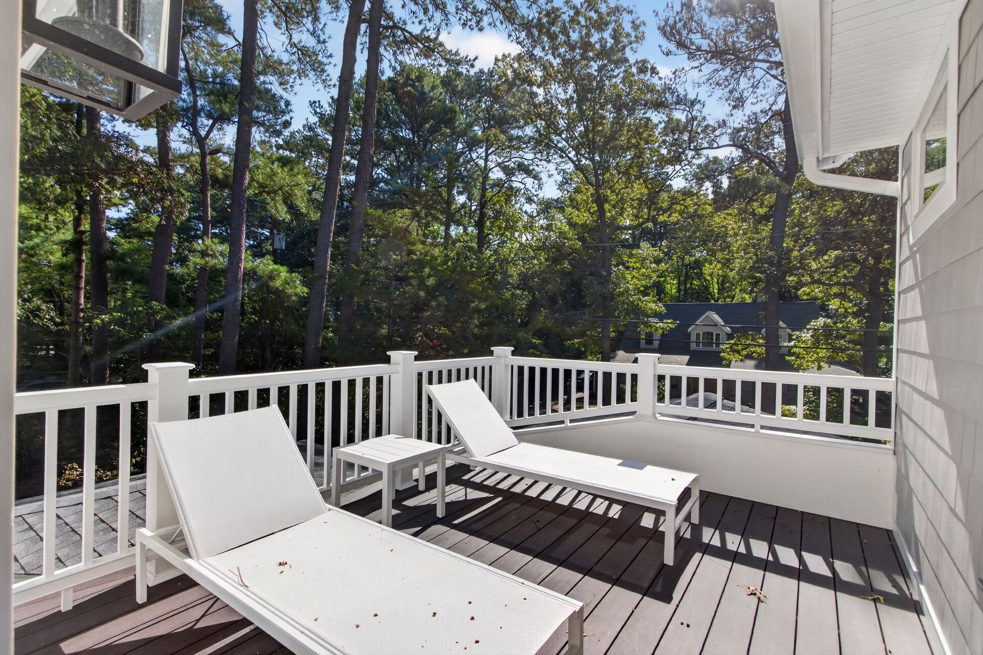 Sunny deck with white lounge chairs, railing, and trees in the background.