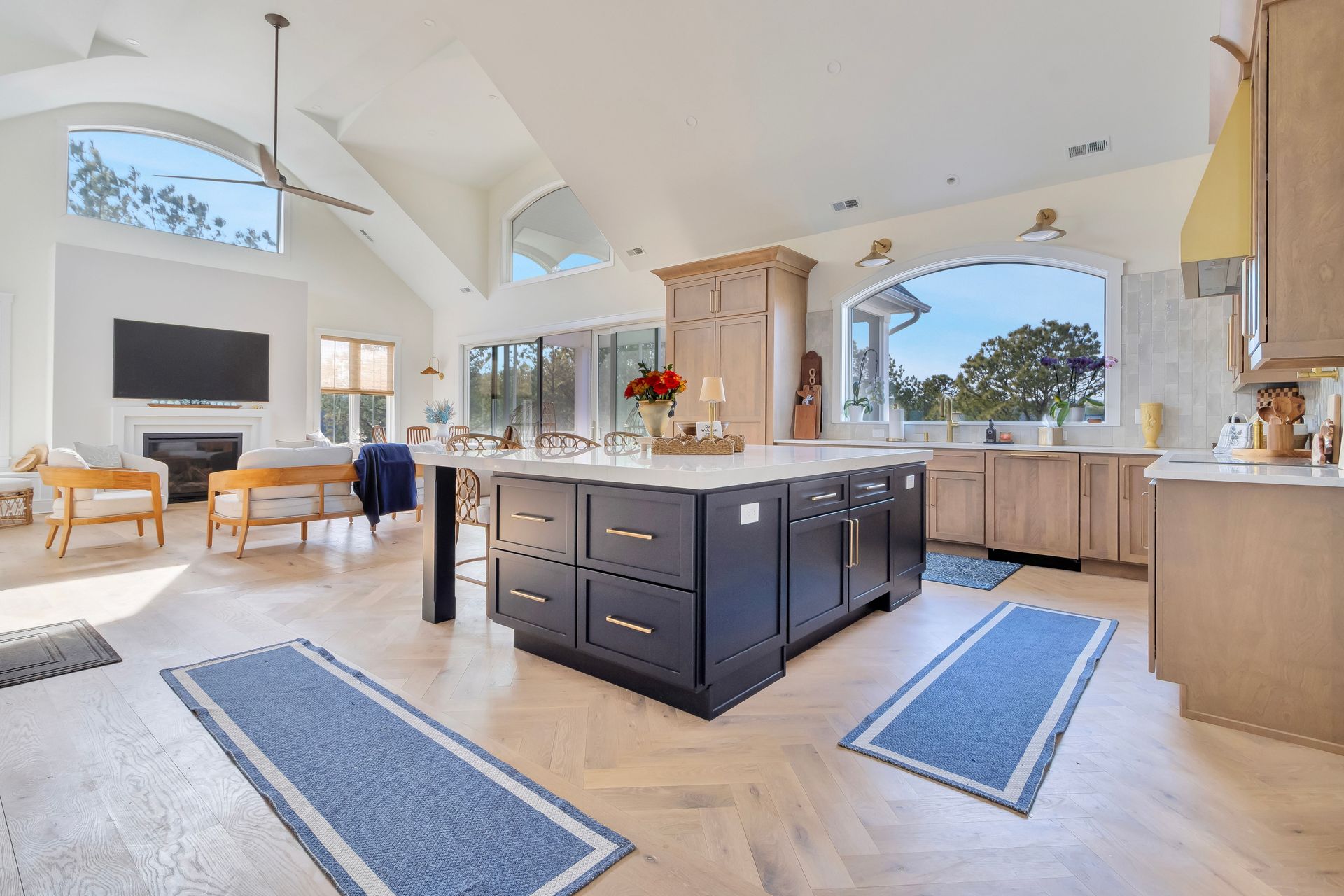Spacious kitchen with a large island, blue rugs, and arched windows. Light wood floors and cabinets.