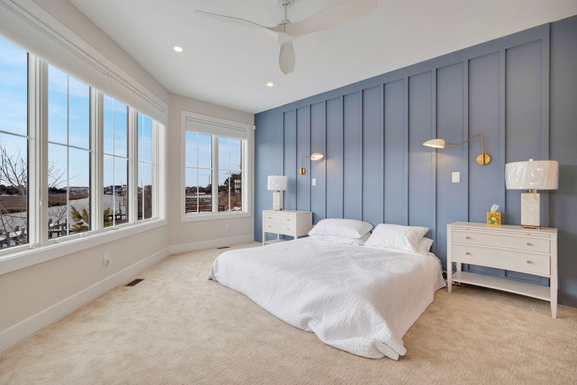 Bedroom with a blue accent wall, large windows, and a bed with white linens.