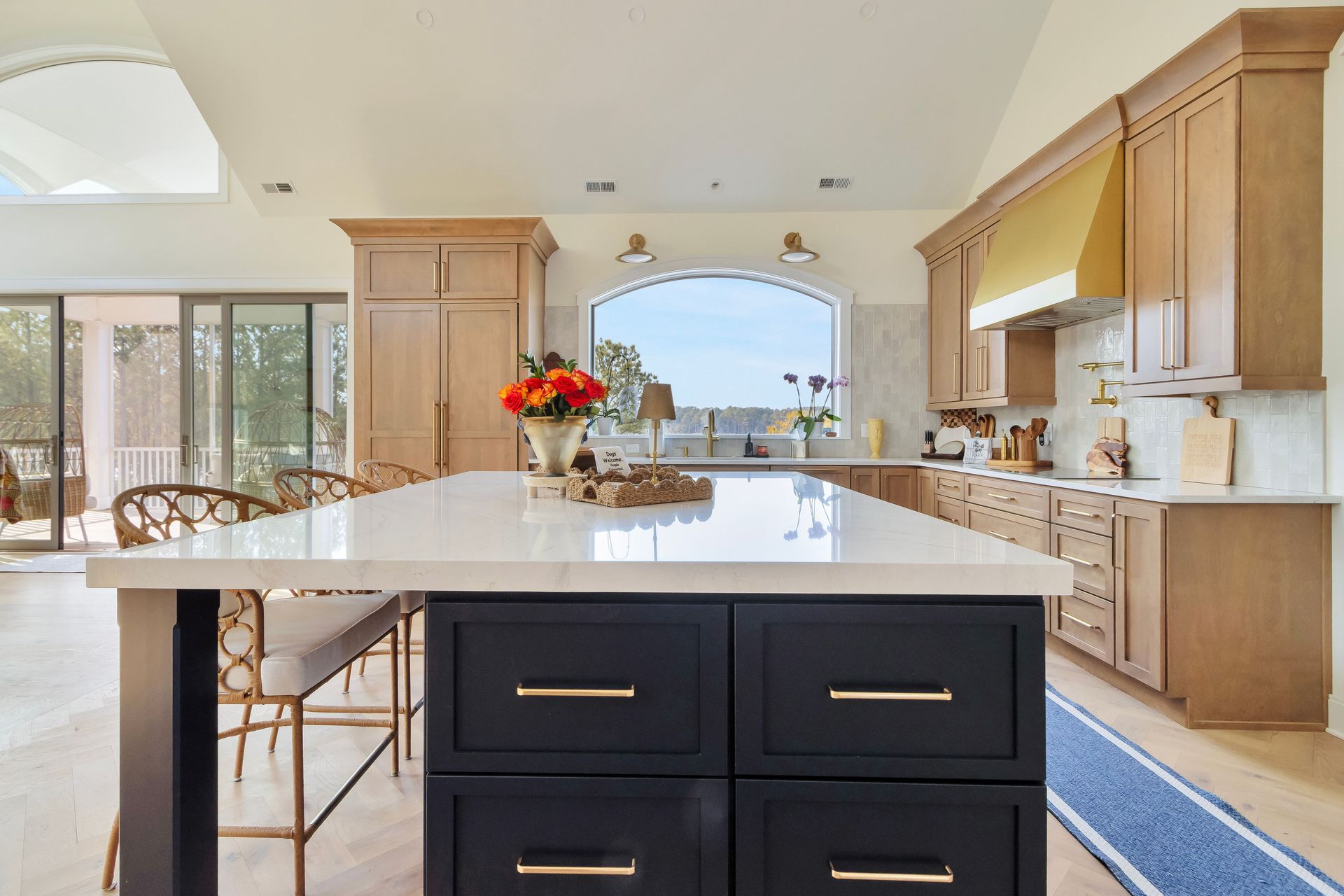 Kitchen with a black and white island, light wood cabinets, and a gold range hood.