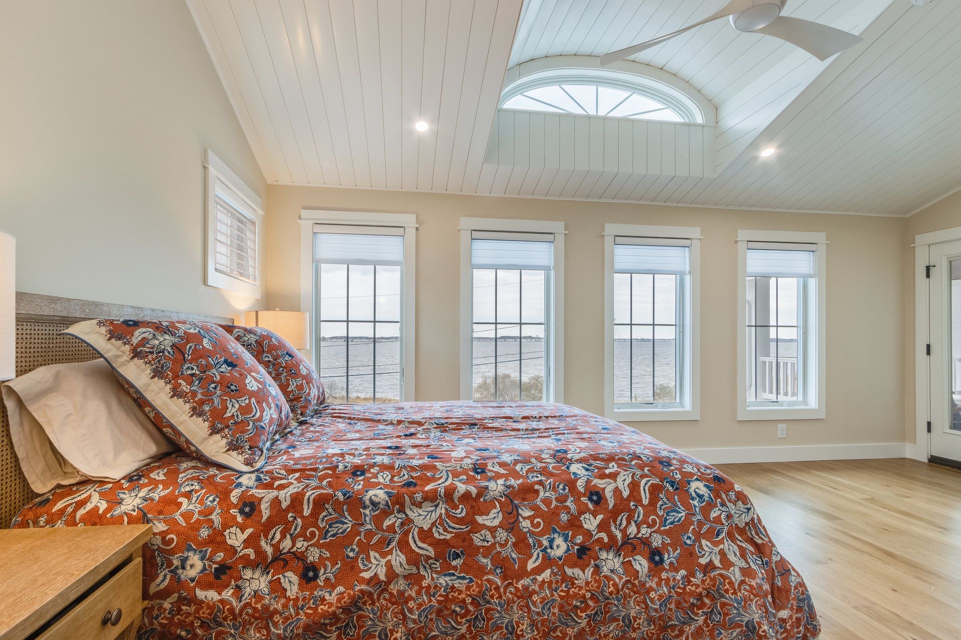 Bedroom with a patterned comforter, three windows, a ceiling fan, and an arched skylight.