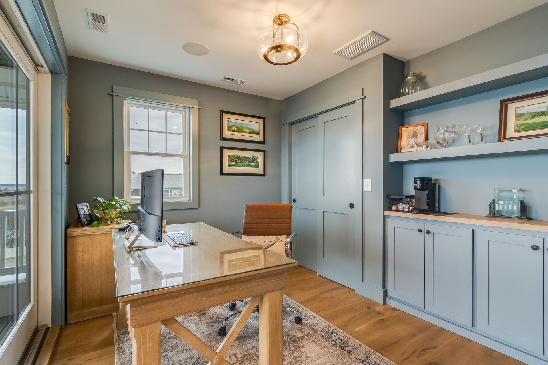 Home office with desk, built-in cabinets, and window, painted blue with wood accents.