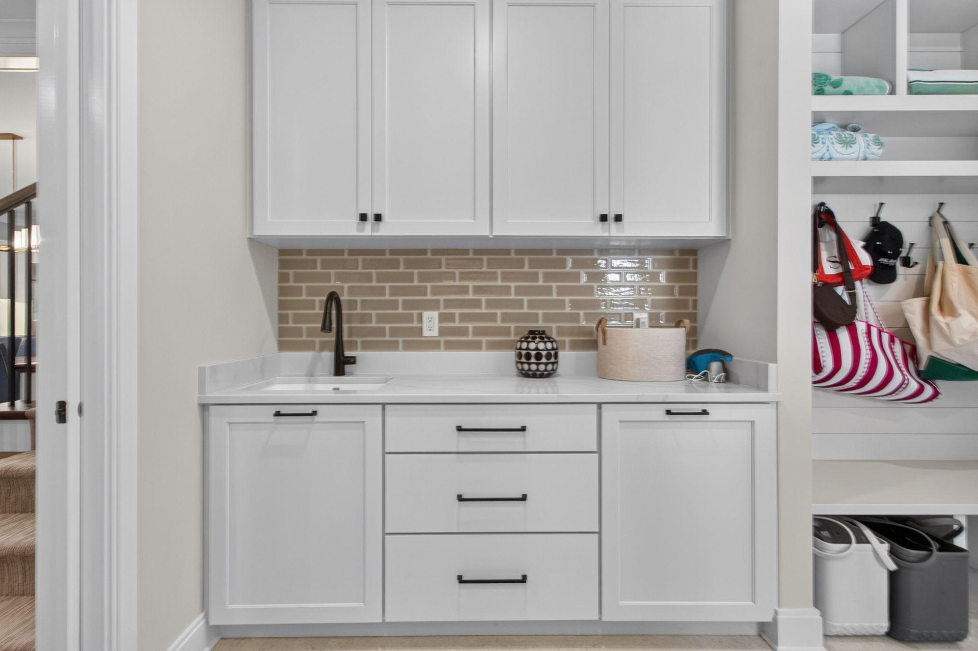 Built-in white laundry room cabinets with countertop, sink, and shelves with folded clothes and baskets