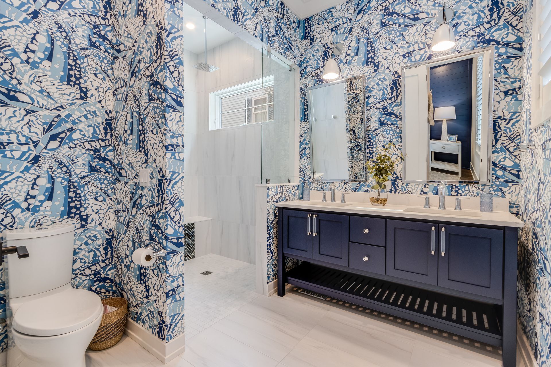 Blue and white floral wallpaper bathroom with a double vanity and a glass shower.
