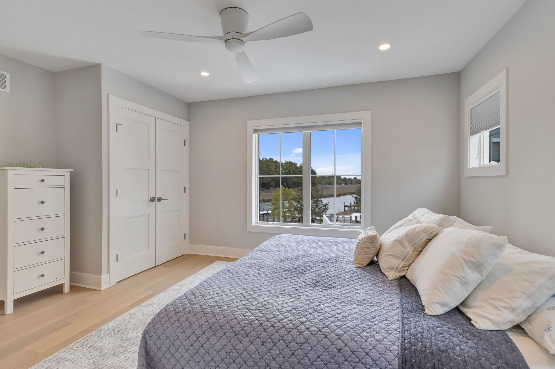 Bedroom with bed, white dresser, window, and closed doors. Light blue and white color scheme.