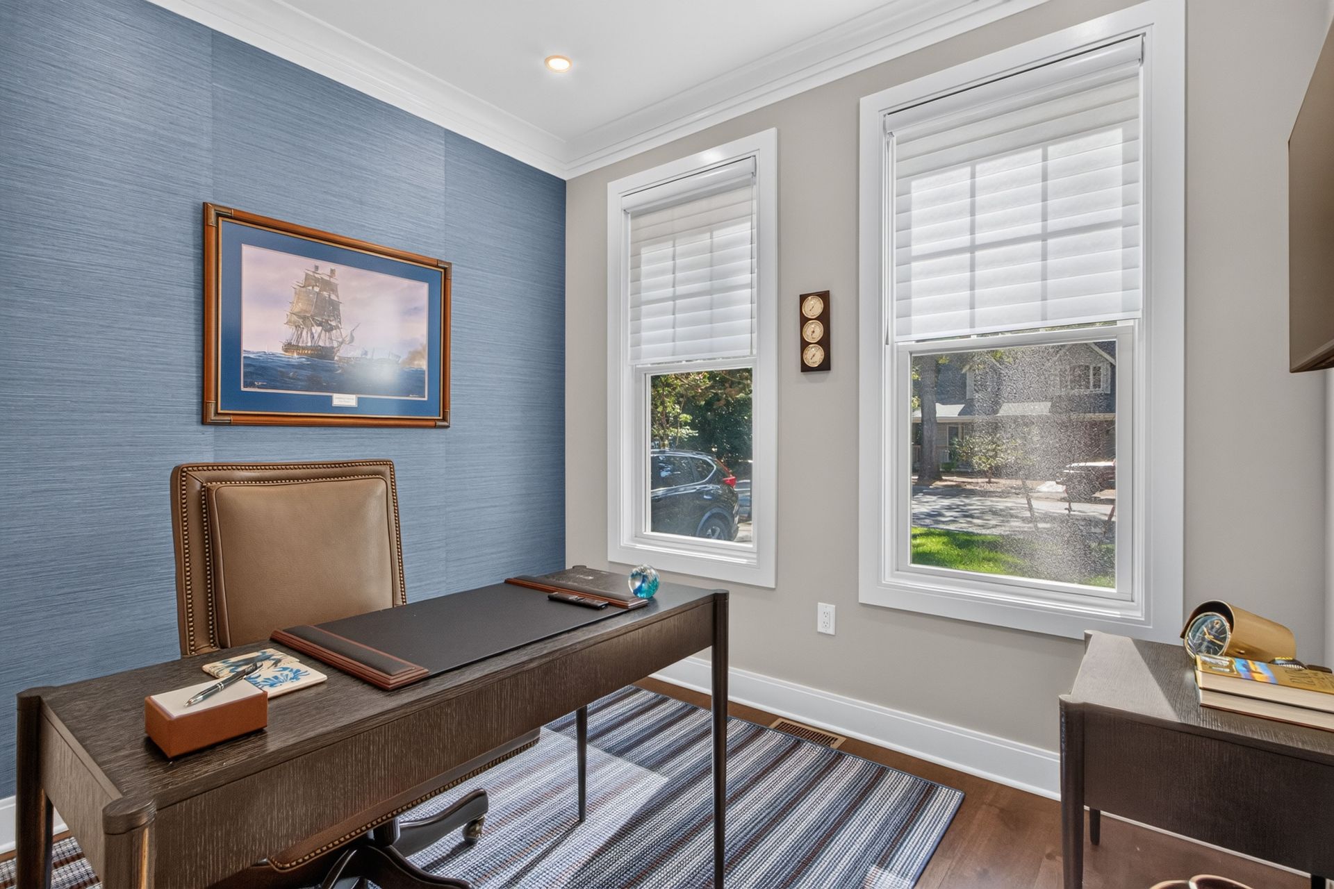 Home office with blue accent wall, desk, chair, windows, and striped rug
