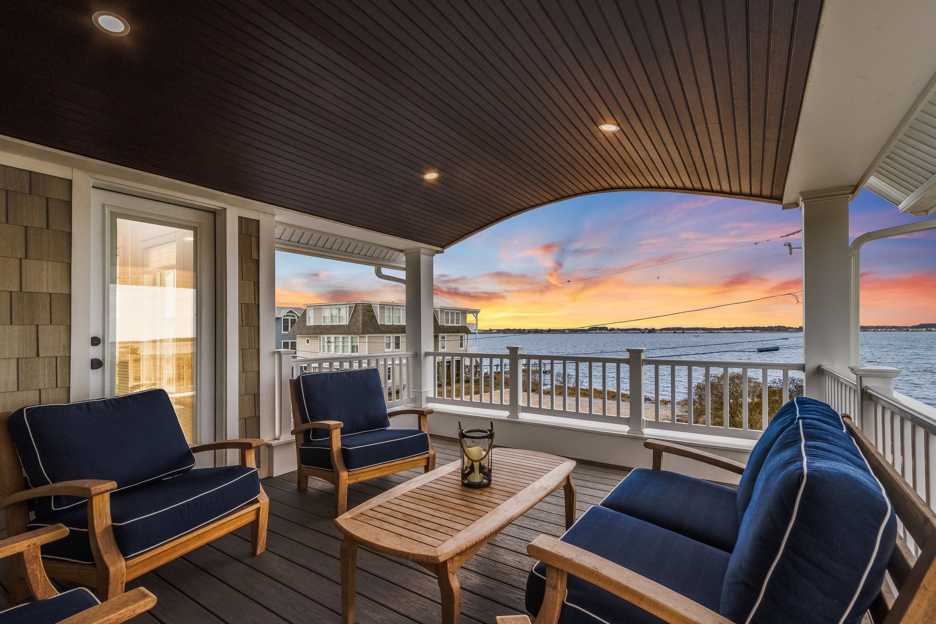 Covered porch with blue chairs, a table, and a waterfront view at sunset.