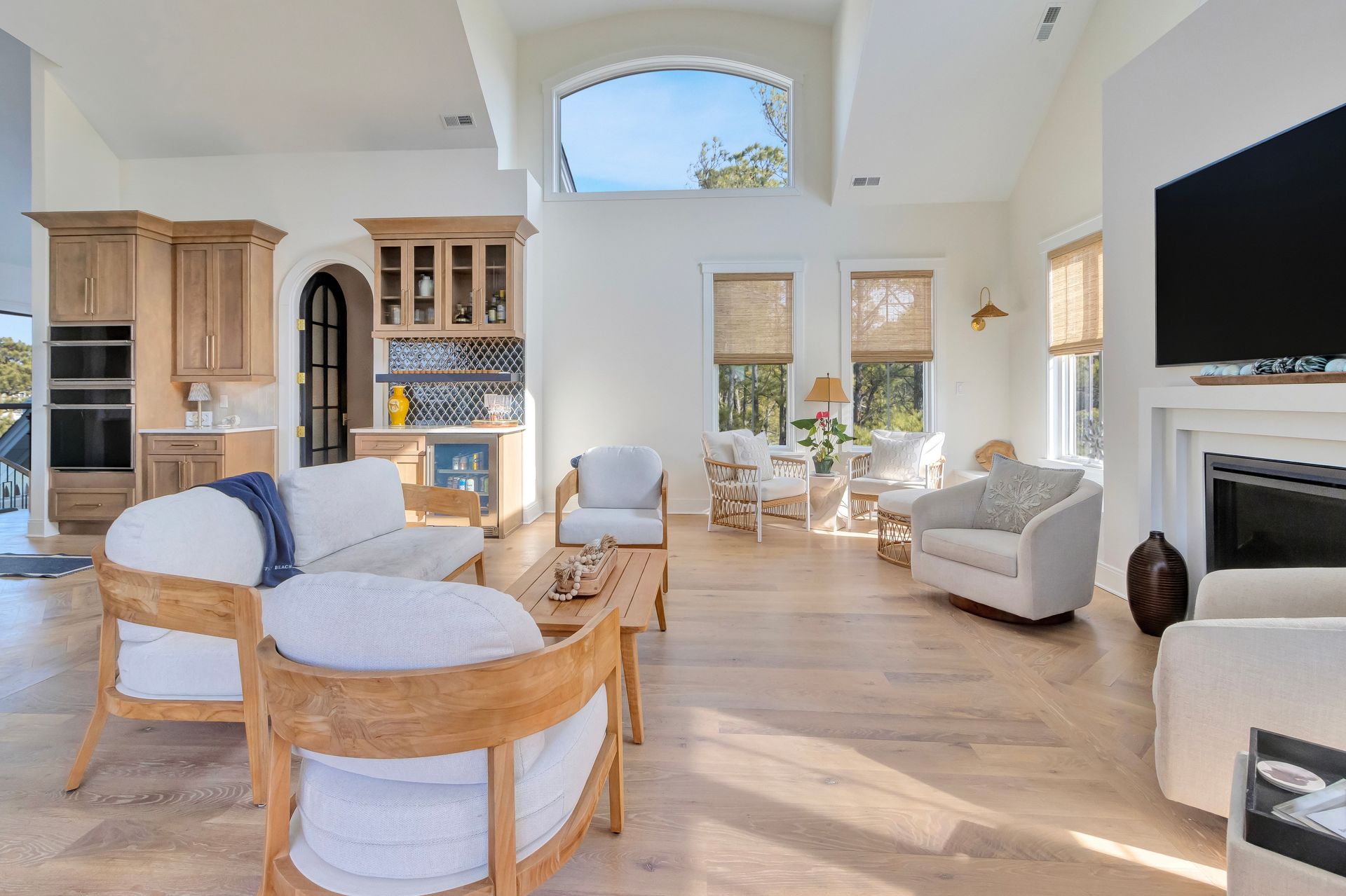 Bright, airy living room with light wood floors, seating, fireplace, and arched window looking out.