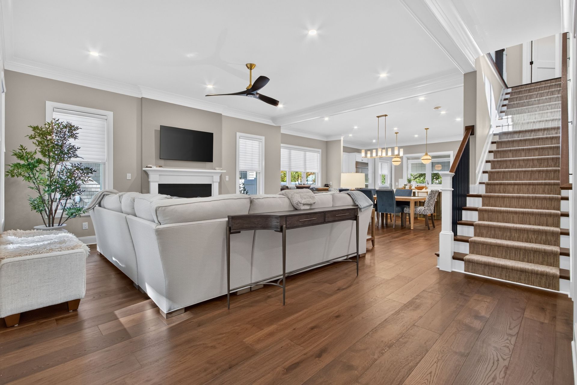 Bright modern open-concept living room with white sectional, wood floors, TV, fireplace, and staircase