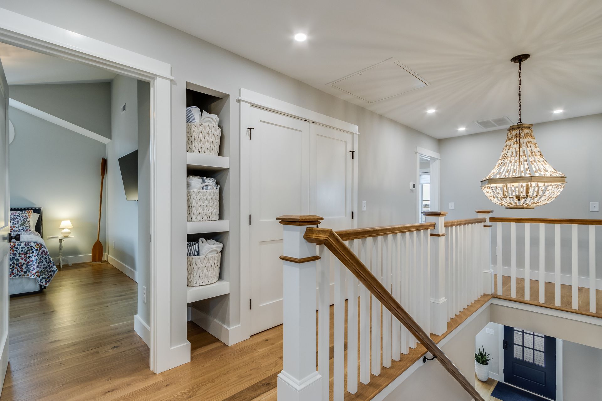 Hallway with built-in shelves, closet, and stairs, featuring a chandelier and view into a bedroom.