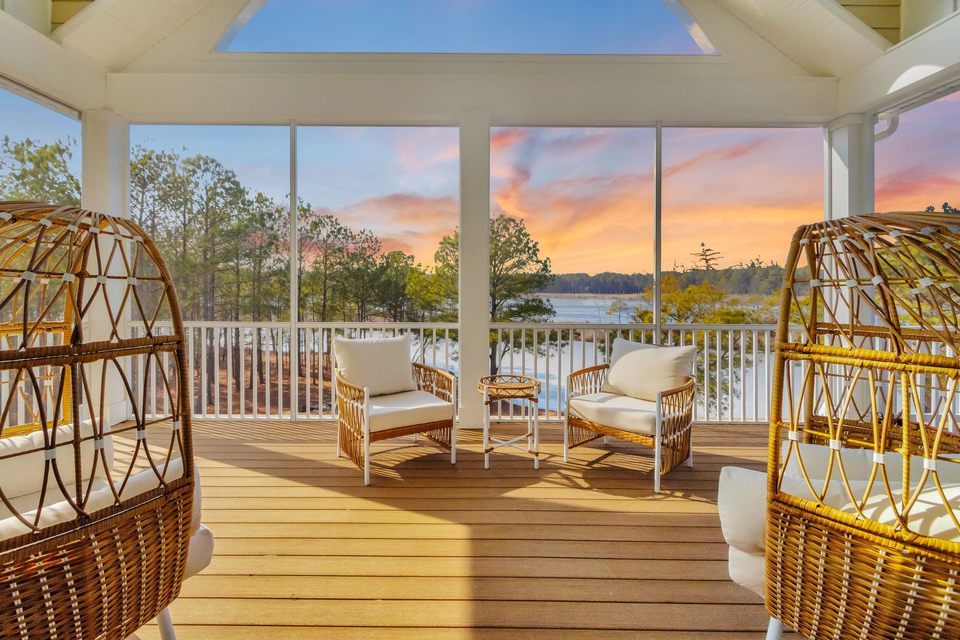 Screened porch with woven chairs, waterfront view at sunset, with orange and purple sky.