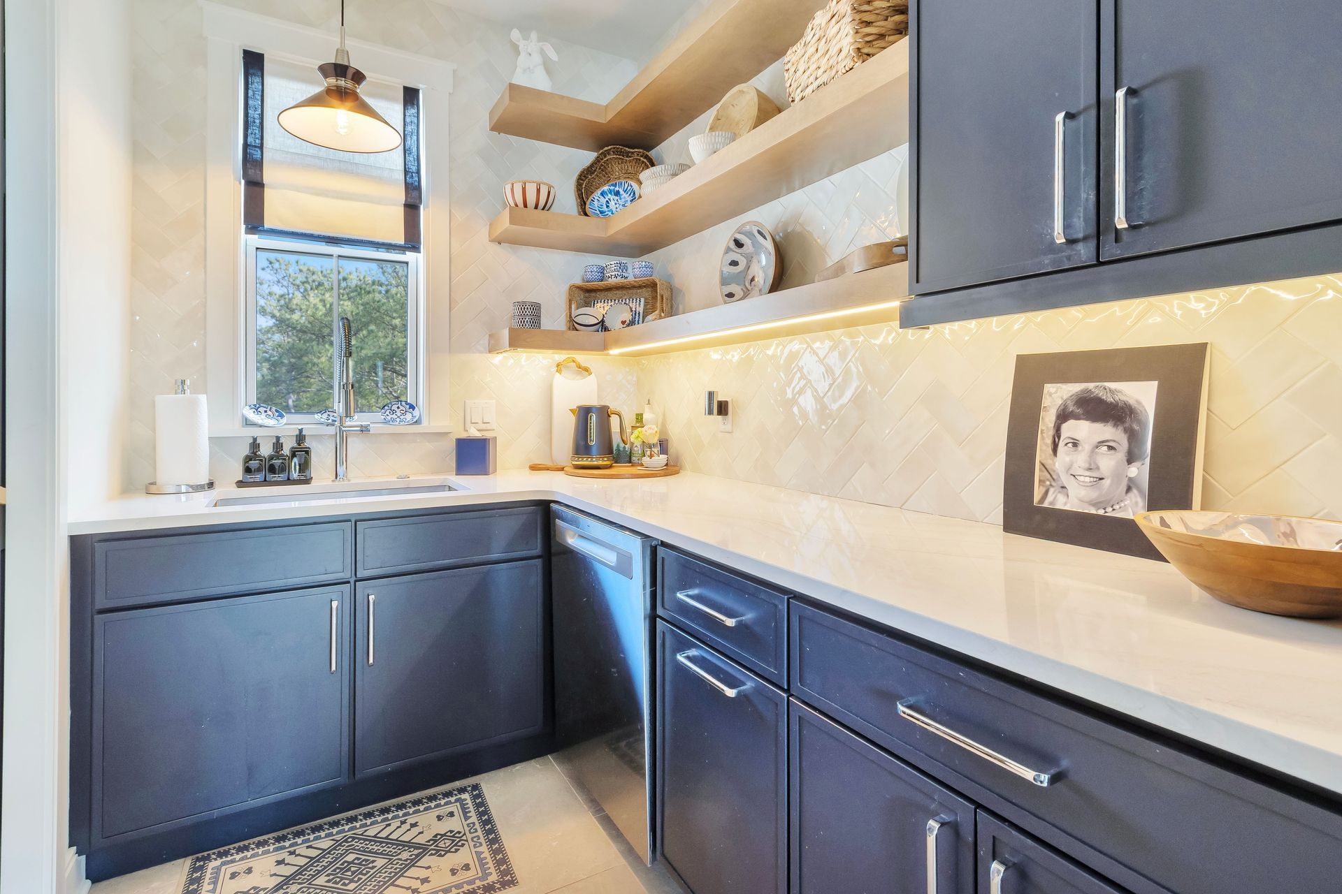 Dark blue kitchen cabinets with white countertops, open shelving, a window, and a photo on the counter.