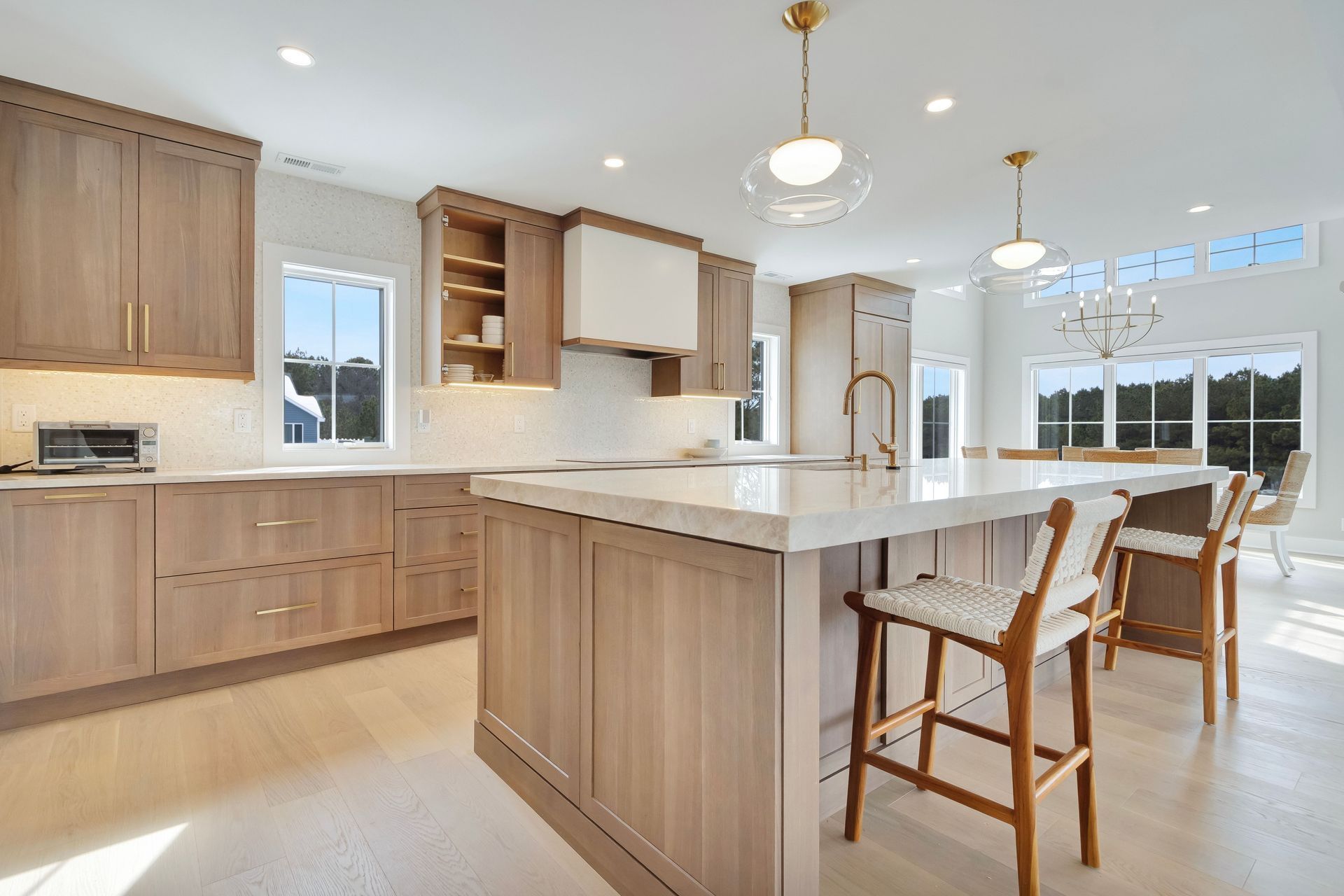 Spacious kitchen with light wood cabinetry, white countertops, island with bar stools, and large windows.