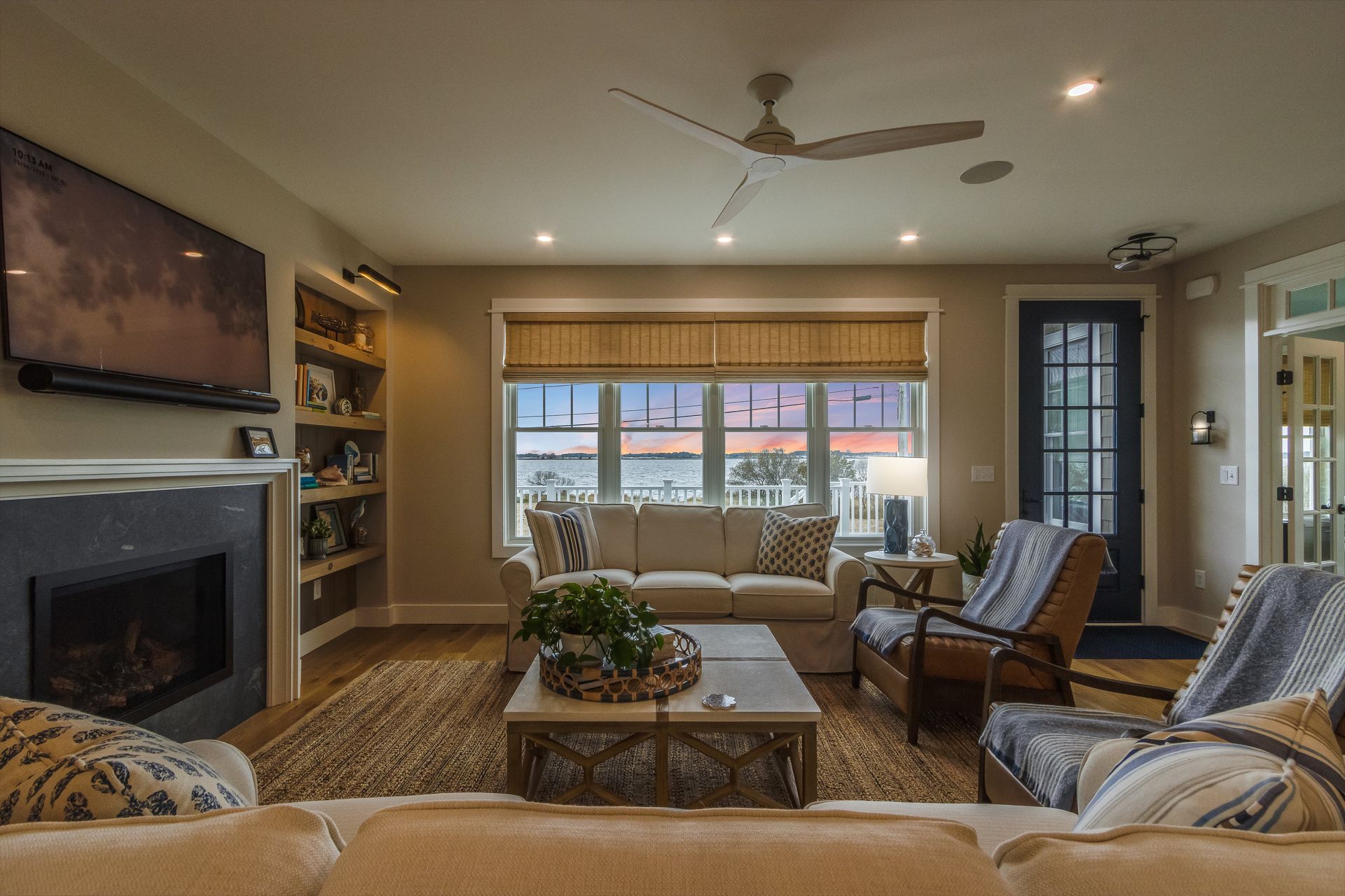 Cozy living room with a fireplace, sofa, chairs, and large window overlooking a colorful sunset.
