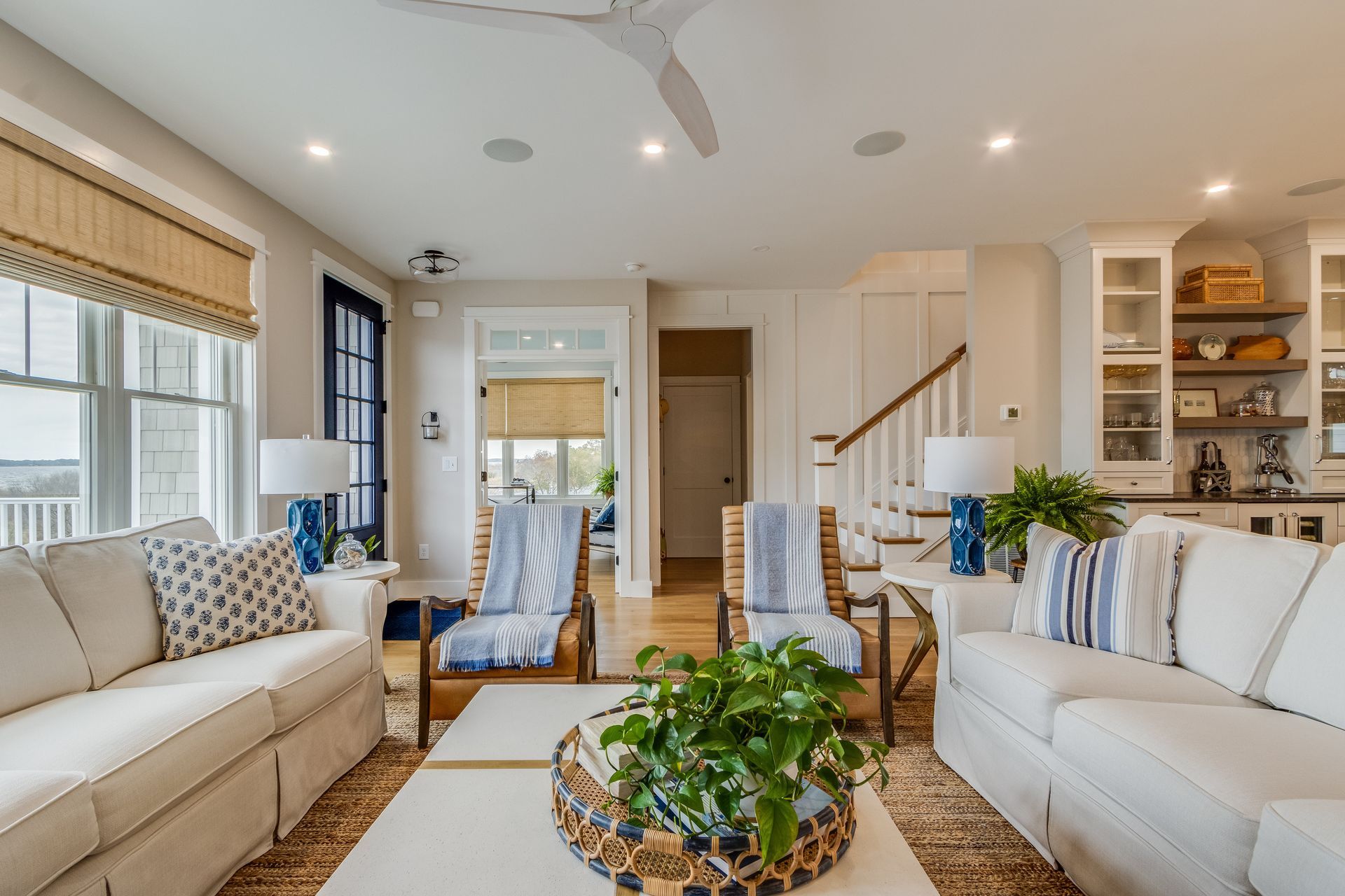 Coastal-style living room with white sofas, blue accents, light wood floors, and a woven rug.