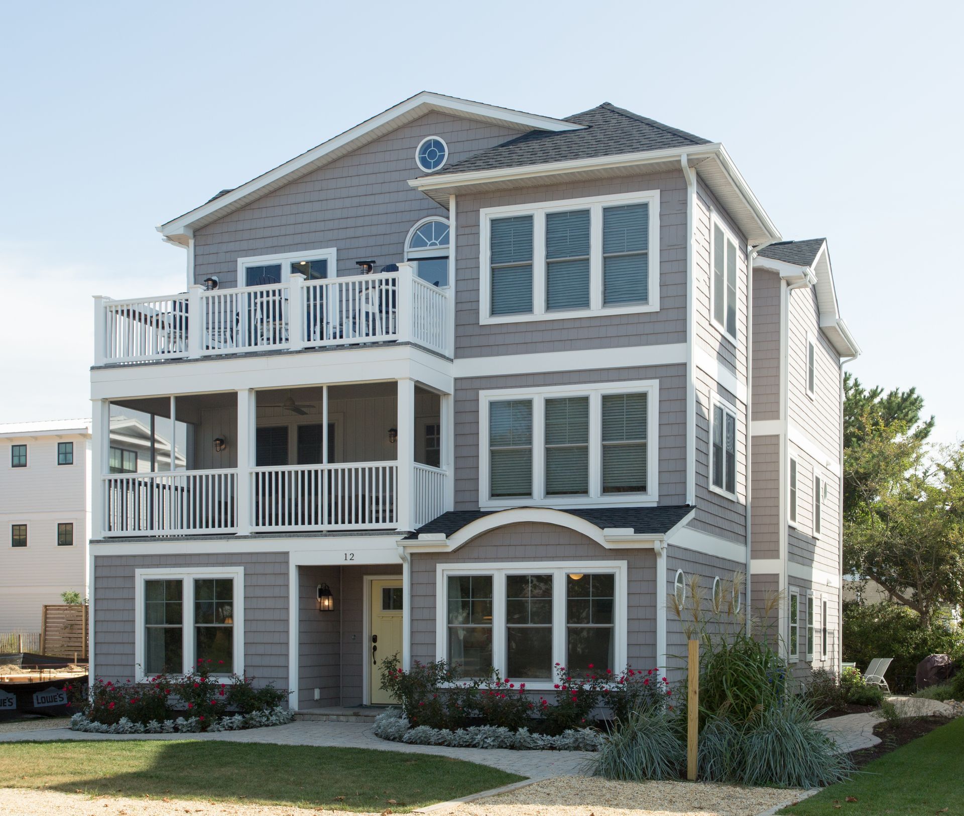 Three-story gray beach house with white balconies and shutters under a bright sky
