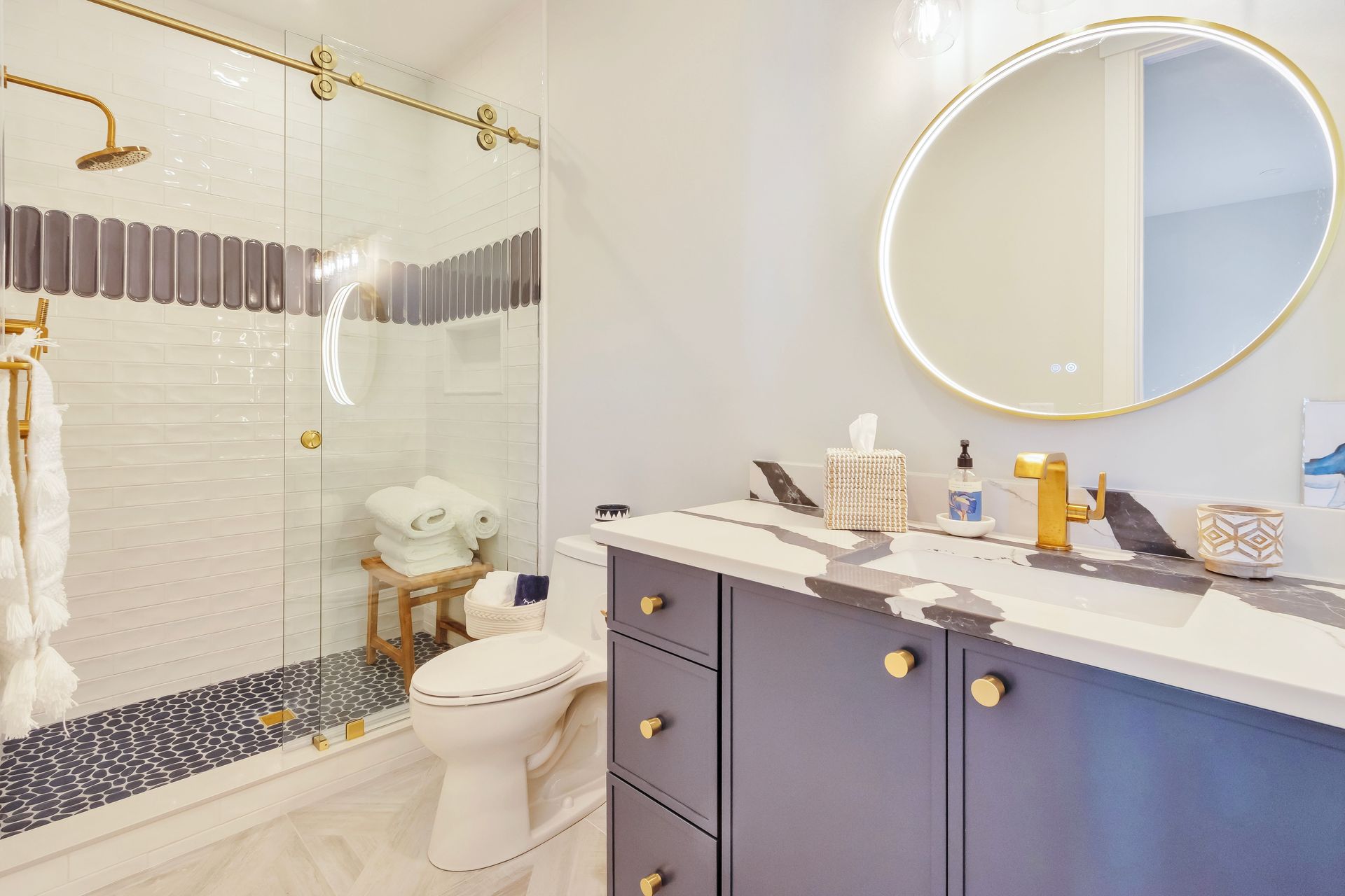 Bathroom with gold fixtures, marble vanity, and glass shower with blue and white tile accents.