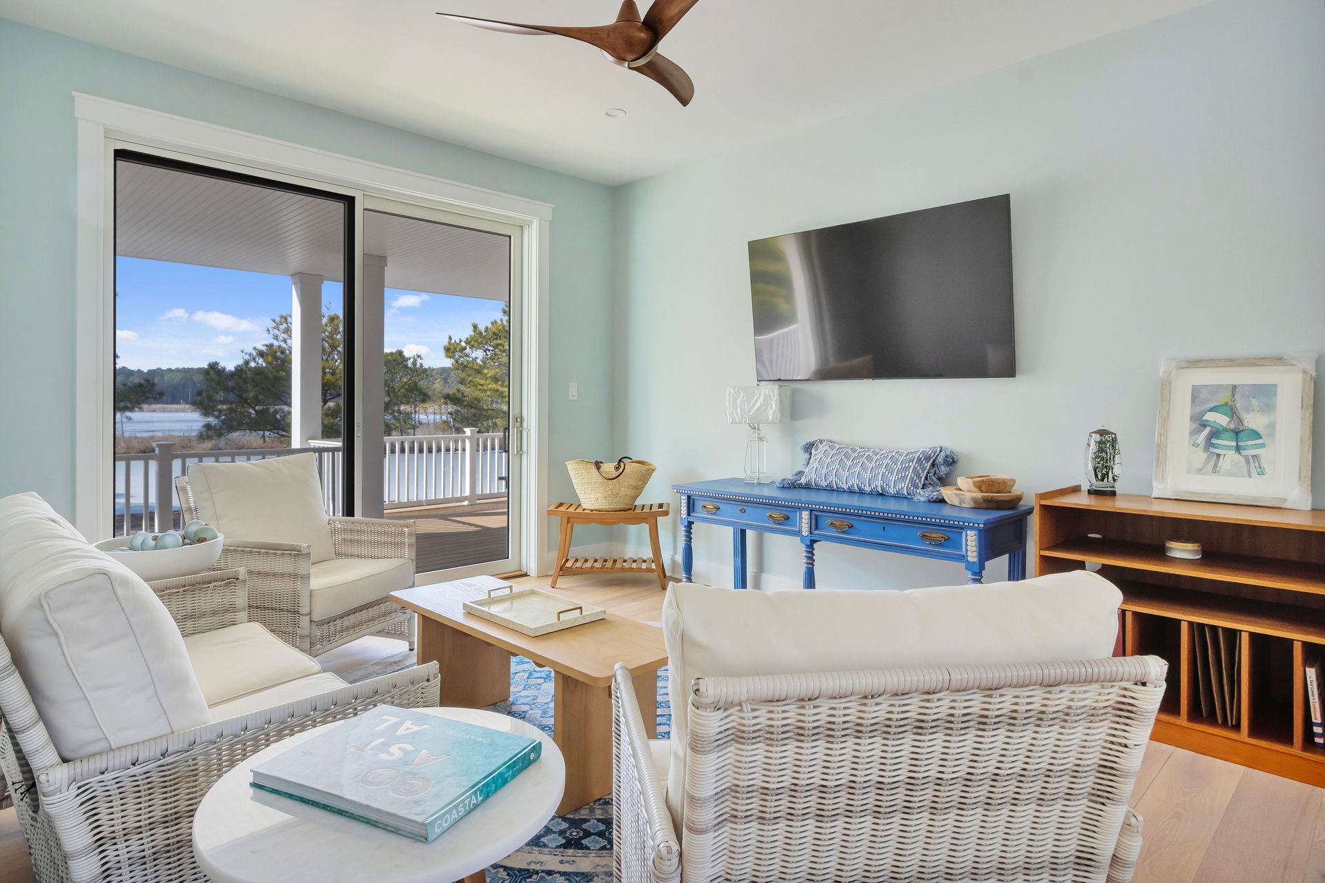 Coastal-style living room with blue walls, white wicker furniture, and a view of a body of water.