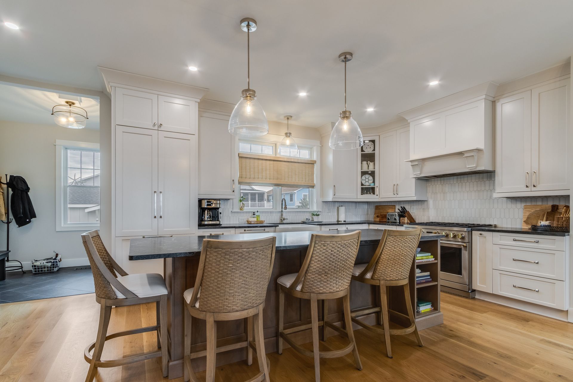 Bright kitchen with white cabinets, dark island, wicker bar stools, and pendant lights.