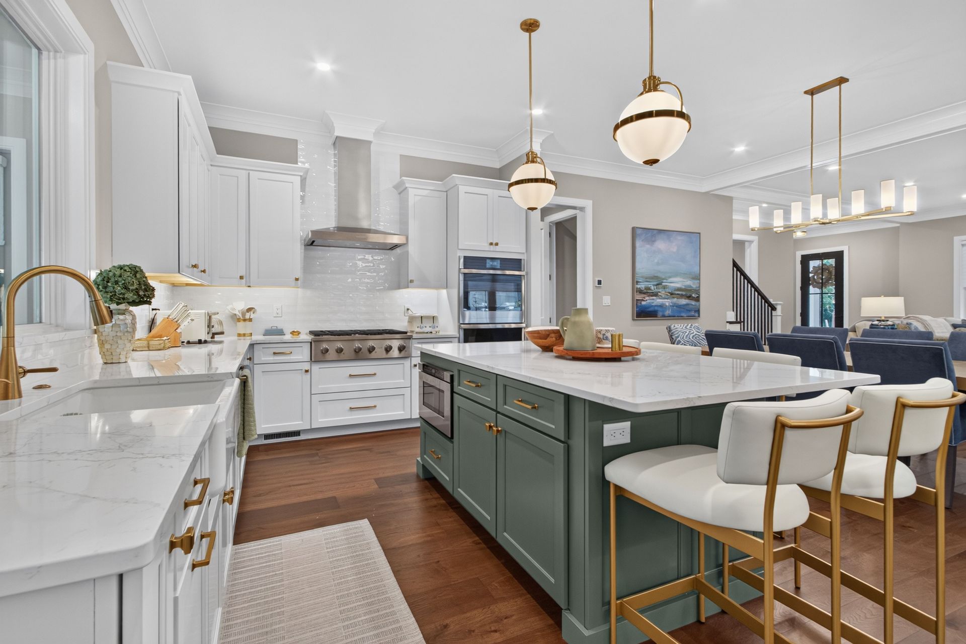 Bright modern kitchen with white cabinets, dark island, brass pendant lights, and wood floors