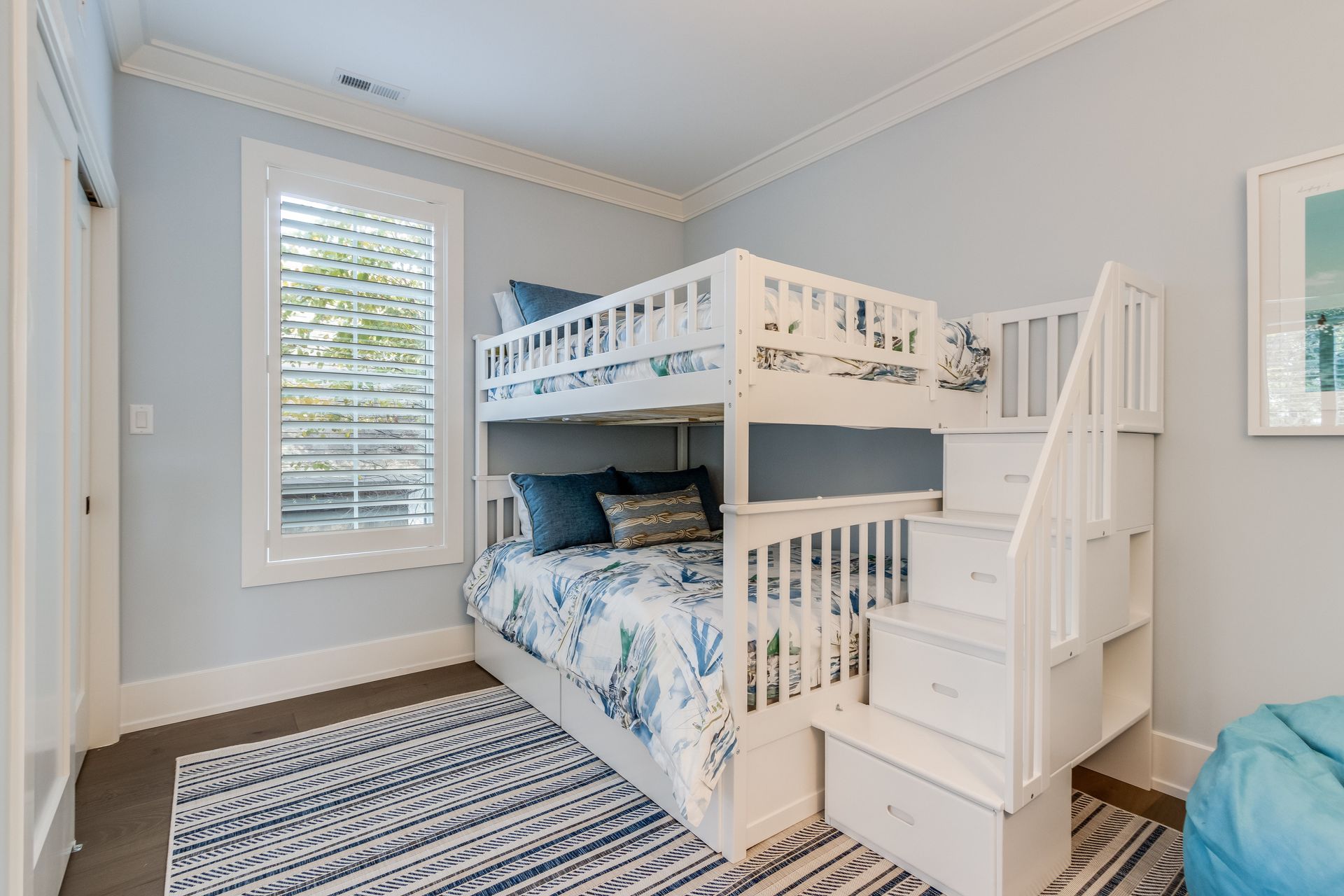 A white bunk bed with a built-in staircase and storage drawers in a room with light blue walls and a patterned rug.