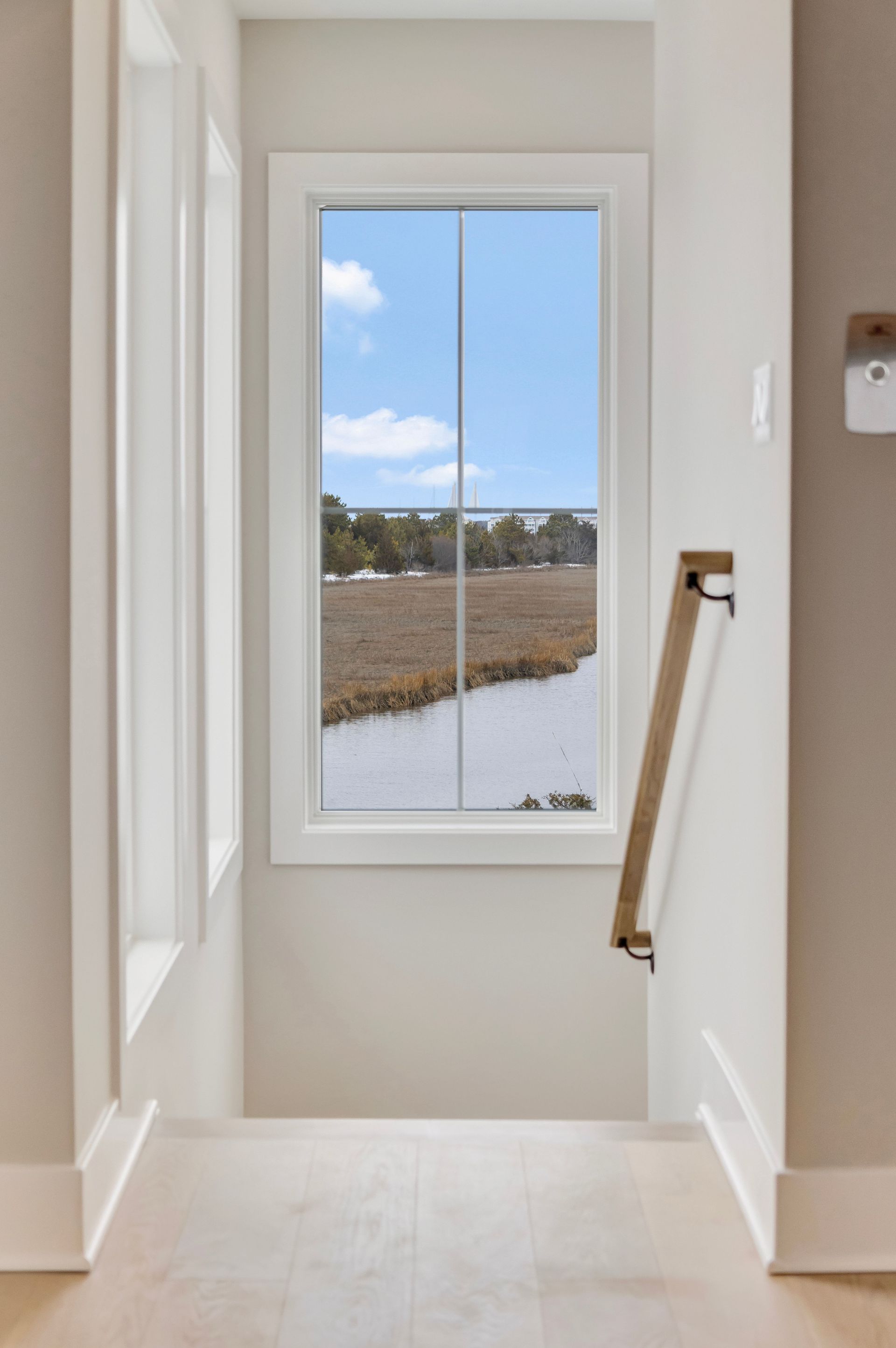 A bright stairway with a large window overlooking a marsh and the sky.
