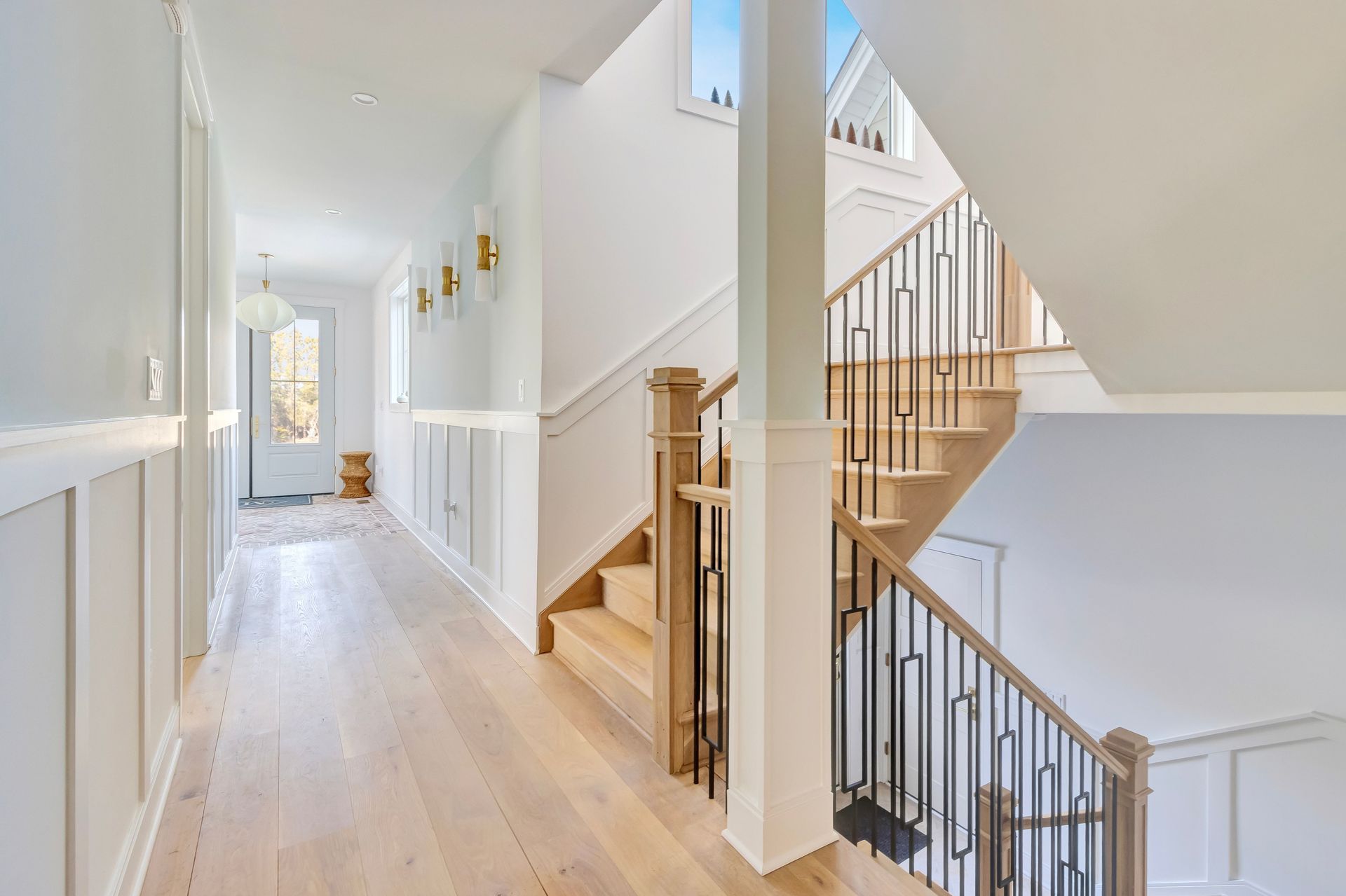Hallway with white walls, wood floors, and a wooden staircase with black railing.