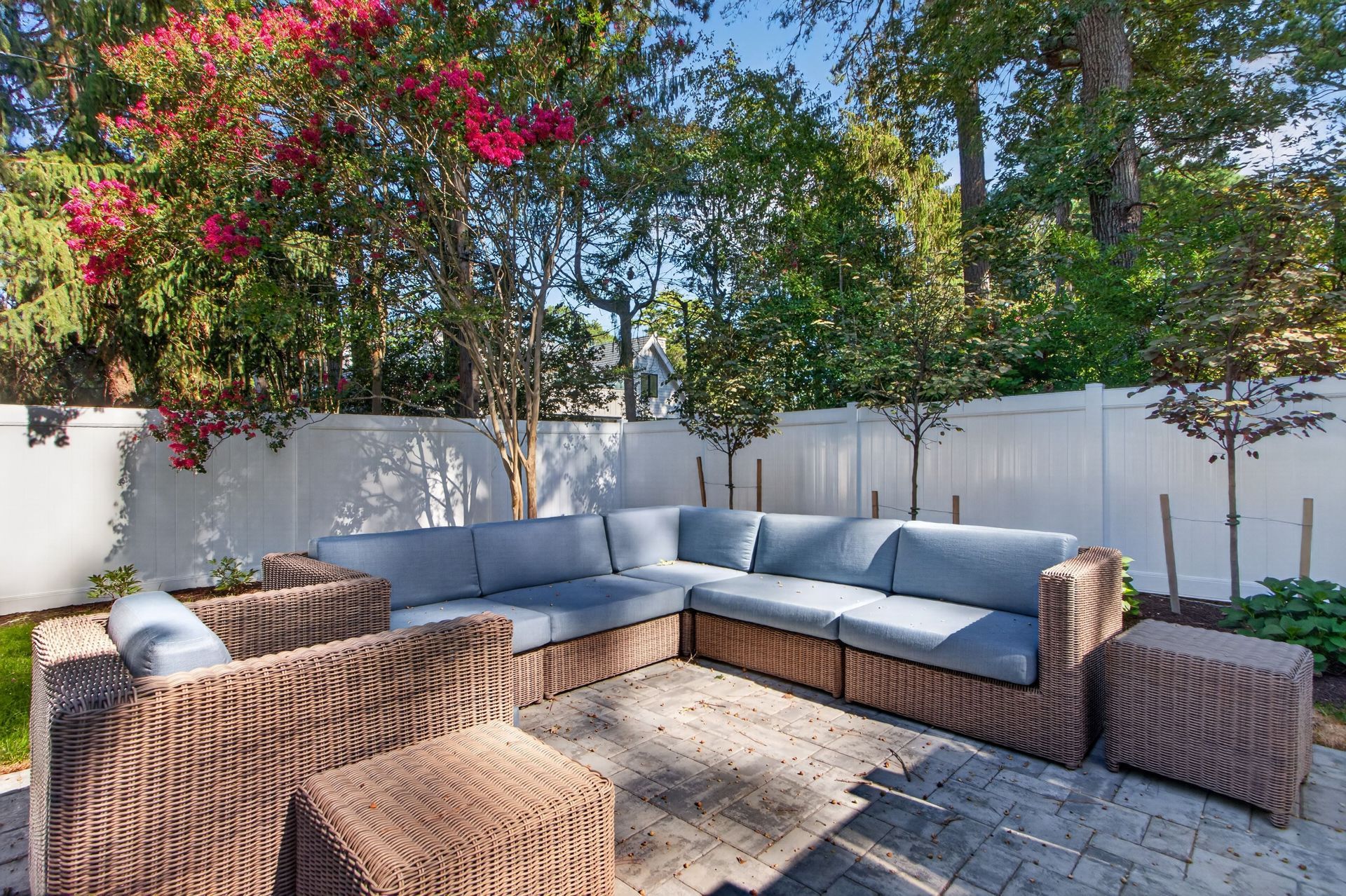 Outdoor patio with gray sectional seating, wicker chairs, and a white fence under flowering trees