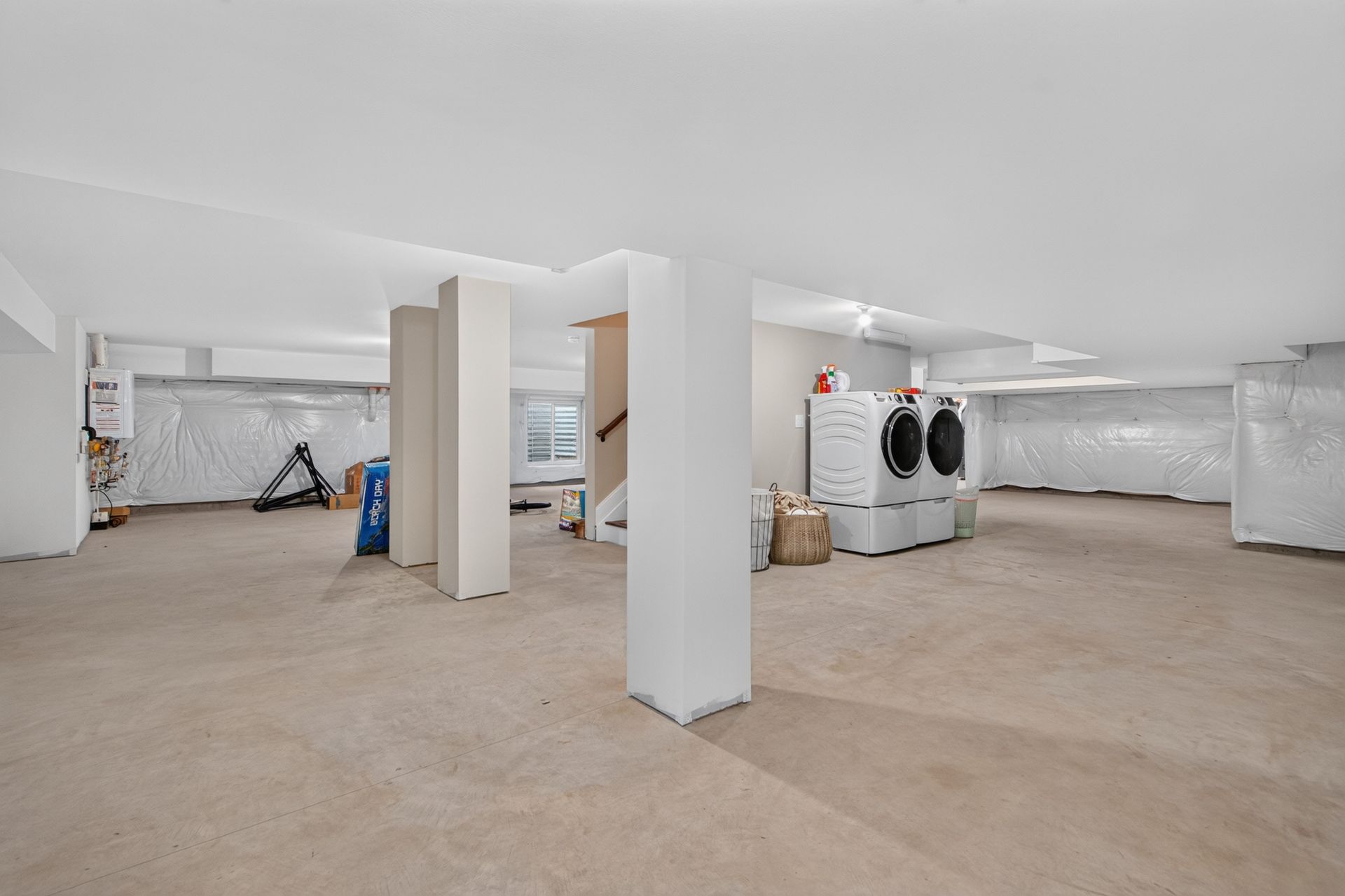Empty unfinished basement with white support columns and laundry appliances in the background