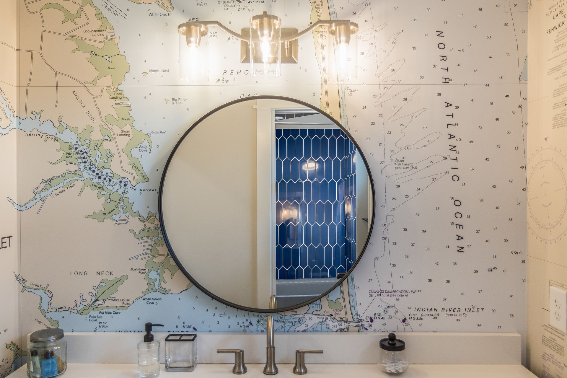 Bathroom vanity with round mirror, map wallpaper, three-light fixture, and sink.