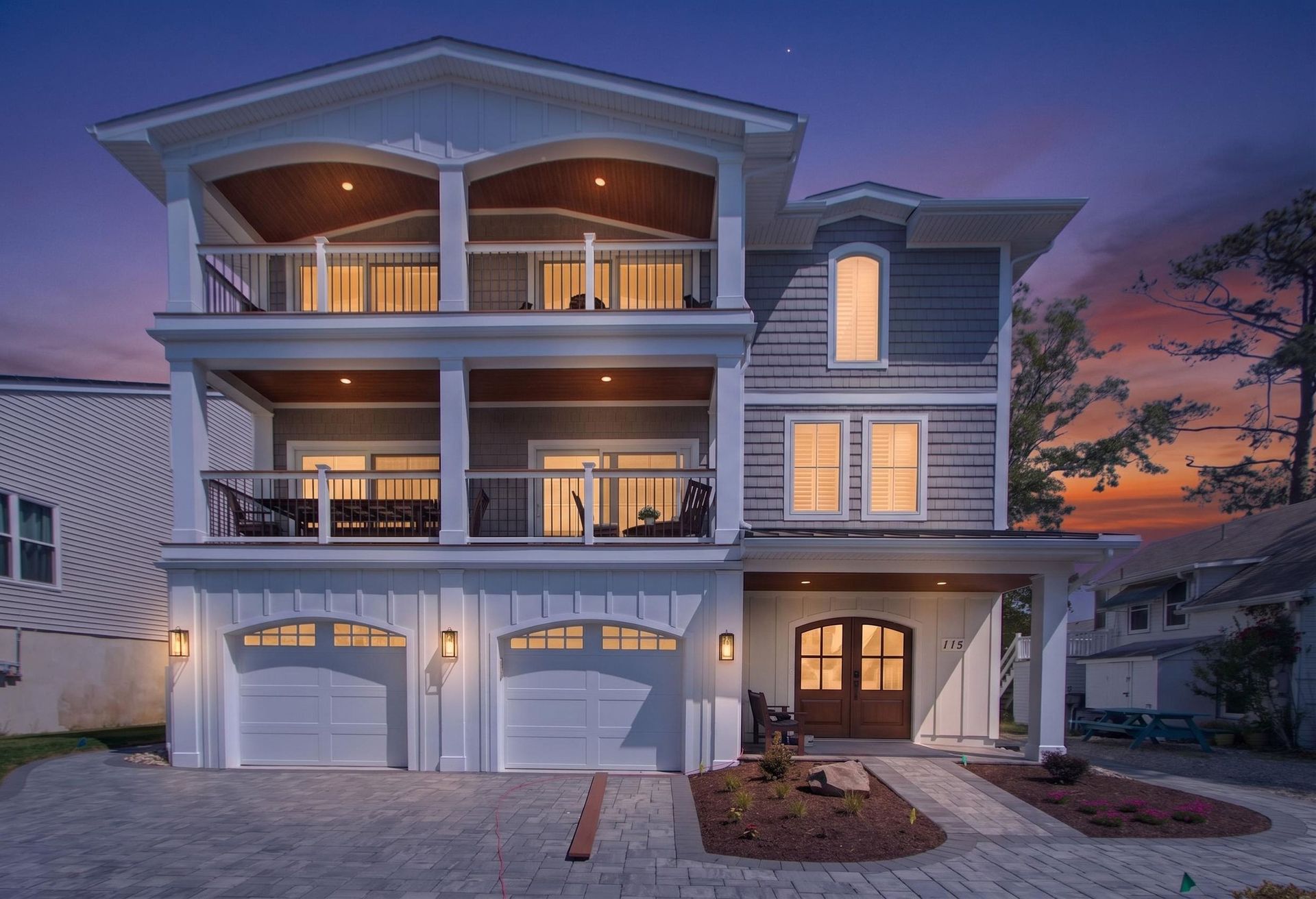 Luxury three-story house with lit balconies and garage at sunset