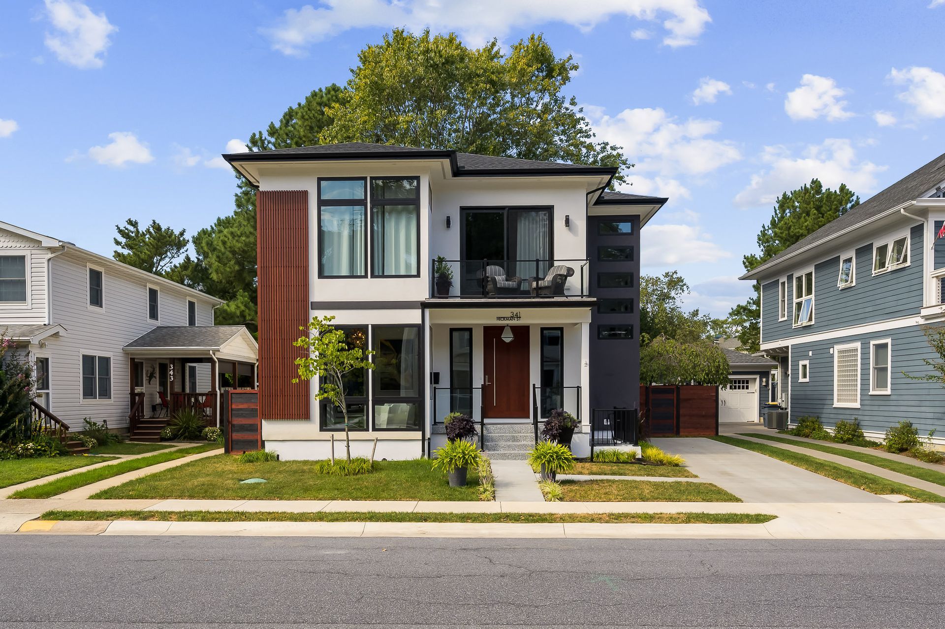 Modern two-story house with brown, white, and gray exterior. Balcony, red door, and driveway.
